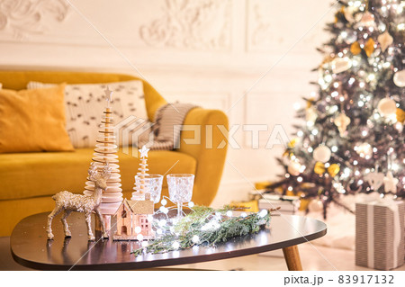 Decorated table in the Christmas interior. Christmas tree. Close-up a small house, Cones, garland, and other Christmas tree toys. light from the garlands 83917132