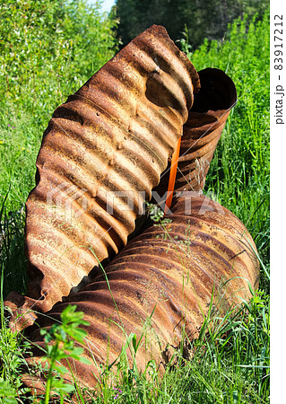A rusty twisted culvert in the grass 83917212