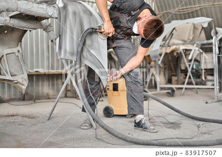 Sanding of car elements. The mechanic works with a grinding tool. Painting car service. Repairing car section after the accident. 83917507