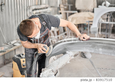 Sanding of car elements. The mechanic works with a grinding tool. Painting car service. Repairing car section after the accident. 83917510