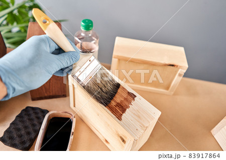 Man carpenter varnishing wooden crate for flowers with brush in her small business woodwork workshop. In your work, do you use stains or wood preservatives to show the wood pattern. Man carpenter varnishing wooden crate for flowers with brush in her small business woodwork workshop. In your work, do you use stains or wood preservatives to show the wood pattern. 83917864