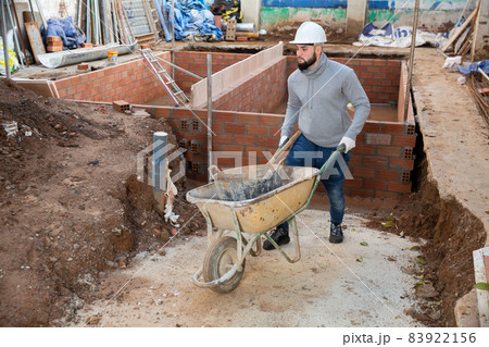 Worker carrying bucket with cement mortar on cart 83922156