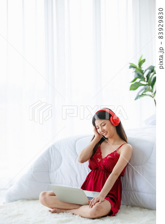Beautiful young naughty sexy girl on red pajamas sit back against white bed end enjoying and think about music listening by earphone and laptop in morning of bright rest day Beautiful young naughty sexy girl on red pajamas sit back against white bed end enjoying and think about music listening by earphone and laptop in morning of bright rest day 83929830