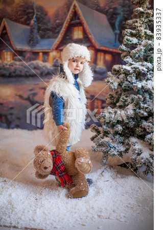 A boy in a white hat and boots on the background of an artificial forest in the winter village A boy in a white hat and boots on the background of an artificial forest in the winter village 83935337