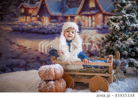 A boy in a white hat and boots on the background of an artificial forest in the winter village A boy in a white hat and boots on the background of an artificial forest in the winter village 83935338