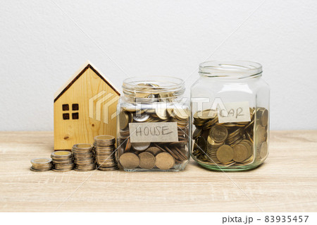 Coin in a glass jar on the brown table with money stack and wooden house, copy space Coin in a glass jar on the brown table with money stack and wooden house, copy space 83935457