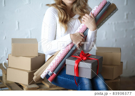 A woman 20-25 years old has bought a lot of boxes and is preparing to pack them in holiday packaging A woman 20-25 years old has bought a lot of boxes and is preparing to pack them in holiday packaging 83936377