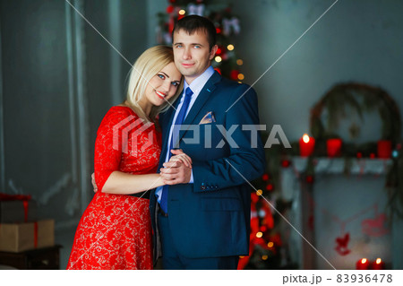 A man gives his beloved woman a gift on new year's eve . The man is dressed in an elegant suit and the woman in a long red evening dress 83936478