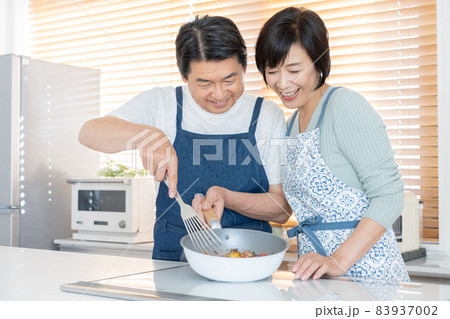 キッチンで仲良く料理をするミドルエイジの夫婦 83937002