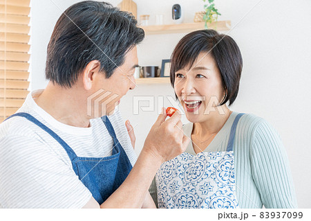 キッチンで奥さんにプチトマトを食べさせるミドルエイジの夫婦の写真素材
