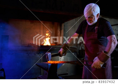 Aged blacksmith forged iron on anvil using heavy hammer 83937432