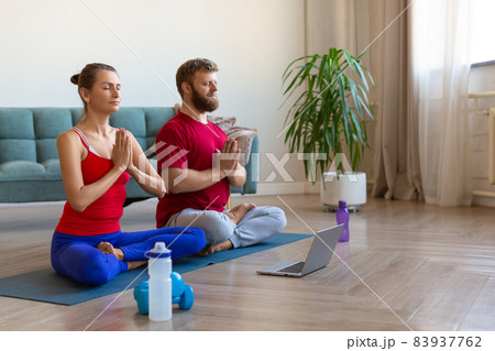 Couple meditating at home with online yoga tutorial. Couple meditating at home with online yoga tutorial. 83937762
