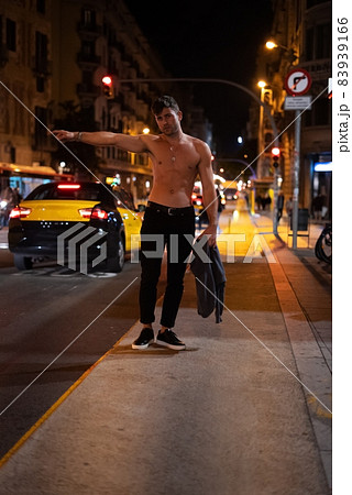 Shirtless guy stretching out arm to hail cab while standing near road on city street at night Shirtless guy stretching out arm to hail cab while standing near road on city street at night 83939166