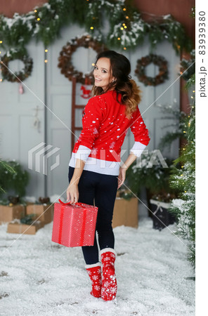 A beautiful young woman in a red sweater stands on the background of Christmas decorations A beautiful young woman in a red sweater stands on the background of Christmas decorations 83939380