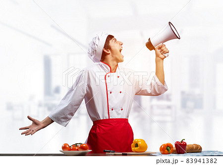 Young chef shouting loudly into megaphone Young chef shouting loudly into megaphone 83941382