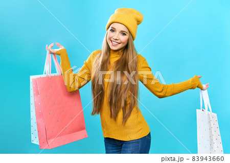 A young woman enjoying her shopping during a big Black Friday sale. Woman with shopping bags. Smiling girl in a yellow hat and yellow sweater on a blue background. A young woman enjoying her shopping during a big Black Friday sale. Woman with shopping bags. Smiling girl in a yellow hat and yellow sweater on a blue background. 83943660