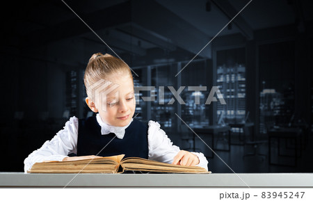 Smiling little girl sitting at desk with open book 83945247