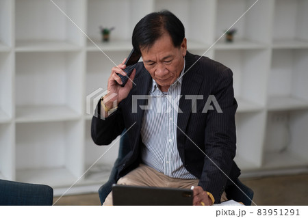 Asian senior manager and businessman in black suit relaxing in social media online and talking, calling with businesspeople on smartphone at workspace in office Asian senior manager and businessman in black suit relaxing in social media online and talking, calling with businesspeople on smartphone at workspace in office 83951291