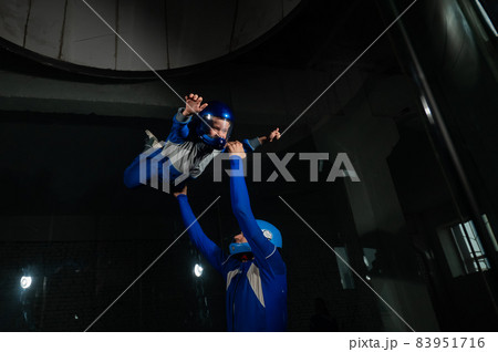 A man teaches a boy to fly in a wind tunnel. 83951716