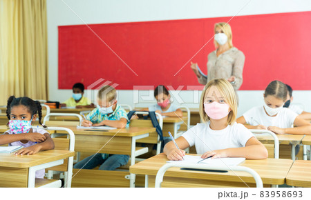 Young girl in protective mask is sitting at the desk in classroom Young girl in protective mask is sitting at the desk in classroom 83958693