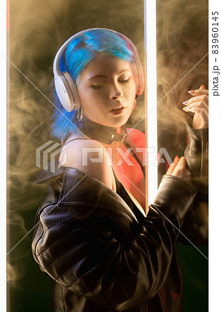 Music vibe. Song chill. Futuristic technology. Inspired gentle cyberpunk woman in headphones enjoying playlist in LED neon light on smoke dark background. Music vibe. Song chill. Futuristic technology. Inspired gentle cyberpunk woman in headphones enjoying playlist in LED neon light on smoke dark background. 83960145