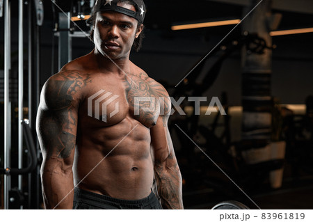 Strong and muscular dark skin man trains on modern equipment in gym. Portrait of muscular pumped up fitness trainer Strong and muscular dark skin man trains on modern equipment in gym. Portrait of muscular pumped up fitness trainer 83961819