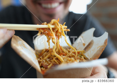 Smiling man eating spicy noodle chinese food with vegetable using chopsticks Smiling man eating spicy noodle chinese food with vegetable using chopsticks 83966360