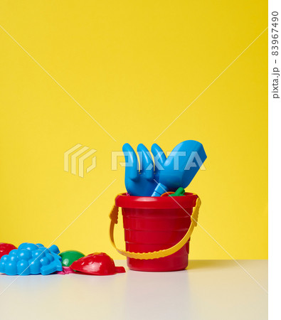 baby red plastic bucket with shovel and toys on a yellow background baby red plastic bucket with shovel and toys on a yellow background 83967490