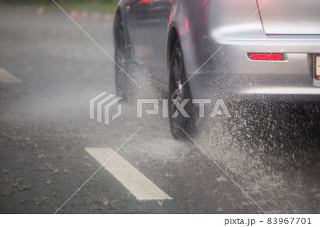 Rain water splash flow from wheels of silver car moving fast in daylight city with selective focus. Rain water splash flow from wheels of silver car moving fast in daylight city with selective focus. 83967701
