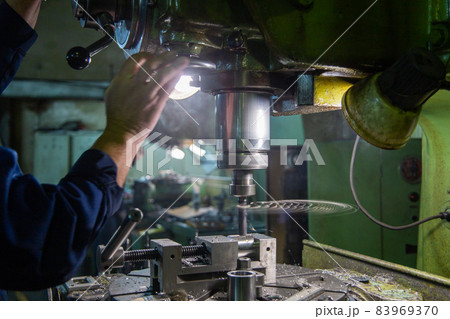 Industrial steel drilling process with smoke. Close-up with selective focus. Manual feed by hand. Workpiece in vise on table. 83969370