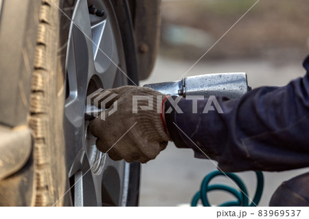 hands of automotive mechanic unscrewing nuts with pneumatic impact wrench during car wheels season changing hands of automotive mechanic unscrewing nuts with pneumatic impact wrench during car wheels season changing 83969537