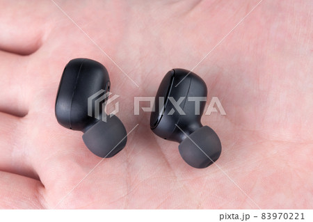 a pair of black wireless earbuds laying on caucasian palm - close-up with selective focus 83970221