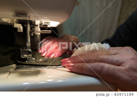 a hand of aged womans with a bandaged finger sews with a sewing machine 83971199