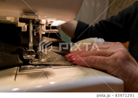 a hand of aged womans with a bandaged finger sews with a sewing machine 83971201