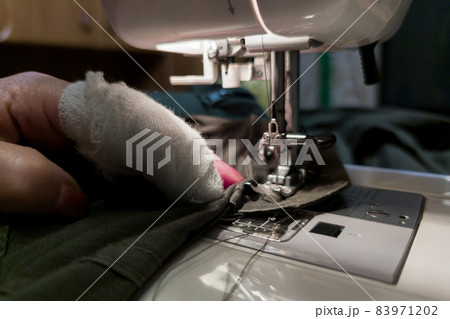 a hand of aged womans with a bandaged finger sews with a sewing machine 83971202