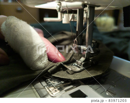 a hand of aged womans with a bandaged finger sews with a sewing machine a hand of aged womans with a bandaged finger sews with a sewing machine 83971203
