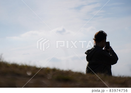 丘の上からスマホで写真を撮る女性 【逆光】 丘の上からスマホで写真を撮る女性 【逆光】 83974756