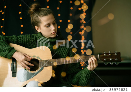 A beautiful teenage girl in Christmas antlers and a green sweater plays the guitar A beautiful teenage girl in Christmas antlers and a green sweater plays the guitar 83975621
