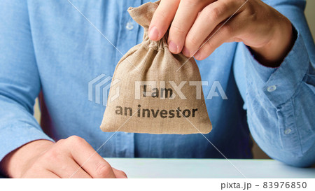 Business investment concept. The person is holding an abstract bag of money with the inscription I am an investor 83976850