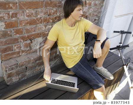 Man sits with laptop and kick scooter in street cafe. Freelancer at work. Student learns remotely from outdoors. Modern lifestyle. Summer vibes. Open air workplace. Man sits with laptop and kick scooter in street cafe. Freelancer at work. Student learns remotely from outdoors. Modern lifestyle. Summer vibes. Open air workplace. 83977343