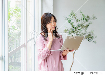 ルームウェアを着て窓際に立ちノートパソコンを操作する女性 83979190
