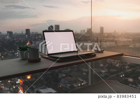 Laptop on the desk at the balcony with evening sunset city view. 83983451