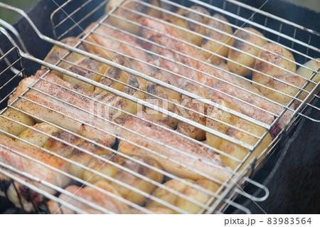 Raw vegetable and slices of meat cooking on grill outdoors 83983564