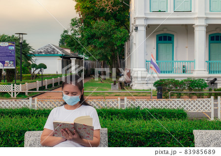 An Asian woman reading a notebook written a long time ago reminded me of the past. In the park wearing a mask to protect it for safety. An Asian woman reading a notebook written a long time ago reminded me of the past. In the park wearing a mask to protect it for safety. 83985689