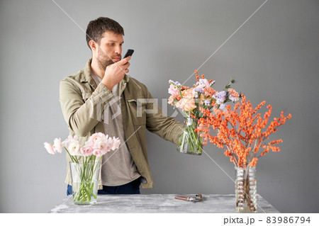 Male florist with a mobile phone, takes a photo to confirm the order. Accepts an online order for flower delivery. Responds to messages in social networks and online messengers. 83986794