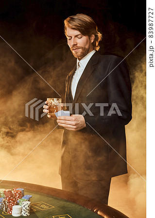 A man in a business suit standing near the game table. Male player. Passion, cards, chips, alcohol, dice, gambling, casino - it is as male entertainment. A man in a business suit standing near the game table. Male player. Passion, cards, chips, alcohol, dice, gambling, casino - it is as male entertainment. 83987727