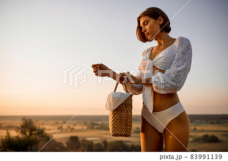 Woman in white lingerie holds basket in the field Woman in white lingerie holds basket in the field 83991139