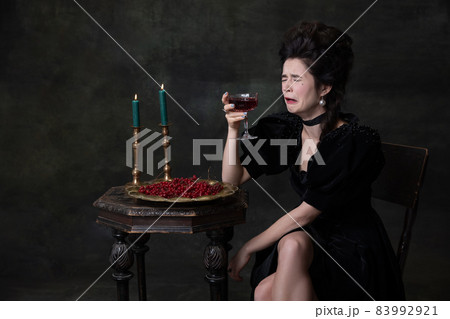 Creative portrait of young beautiful woman in black holiday attire drinking wine alone and crying isolated on dark vintage background. Creative portrait of young beautiful woman in black holiday attire drinking wine alone and crying isolated on dark vintage background. 83992921
