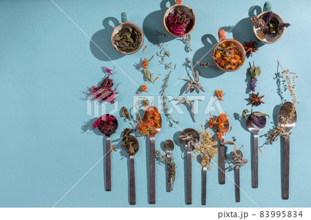 Assortment of dried relaxing tea herbs in spoons and cups  on blue background. Calendula, mint, anise hyssop, monarda didyma, wormwood, sage leaves. 83995834