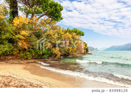 Autumn beach on Lake Garda overlooking the Alps slightly covered with snow 83998126